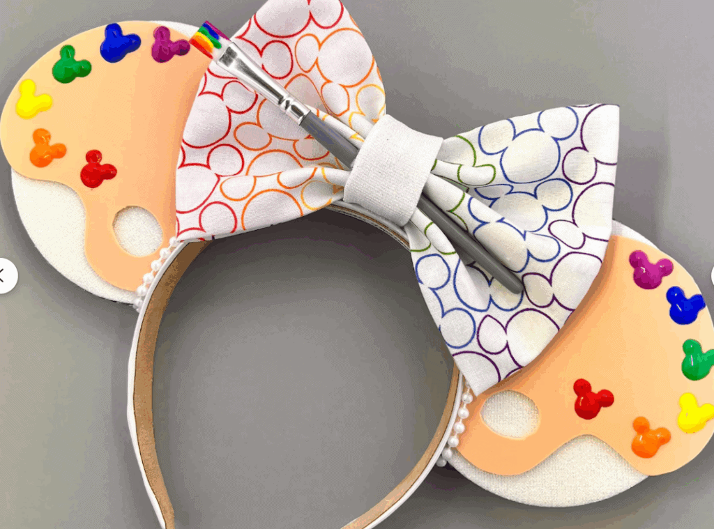 Colorful Disney Mickey Mouse ears headband with rainbow-themed bow, paint palette, and Disney-inspired design.