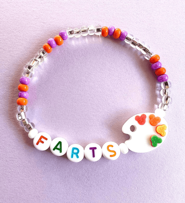 Colorful beaded bracelet with "FARTS" spelled out in letter beads and a white palette charm with heart-shaped paint splashes.