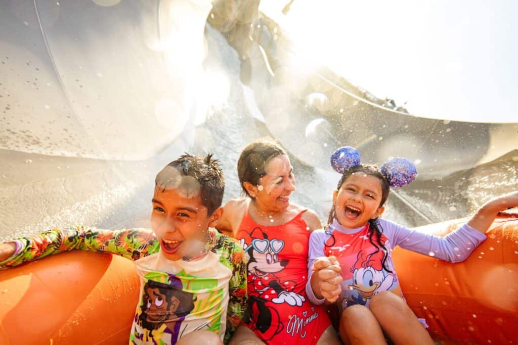 Children enjoying a water ride with Disney-themed swimsuits, smiling, and splashing water at a theme park.