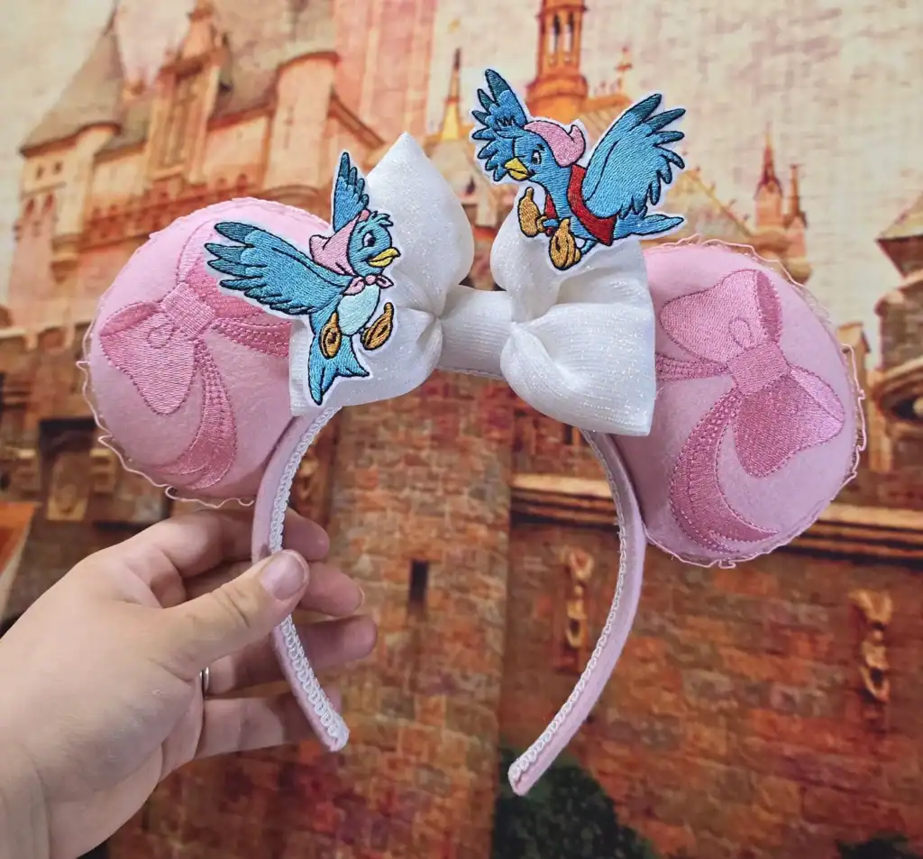 Vintage-inspired Disney Minnie Mouse ears headband featuring embroidered Daisy Duck patches and pink satin bows.