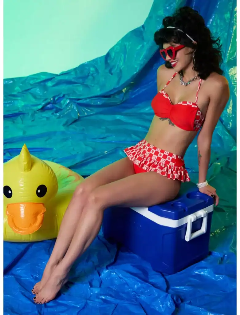 Woman in red Disney-themed swimsuit with ruffle, sunglasses, and accessories at the beach.