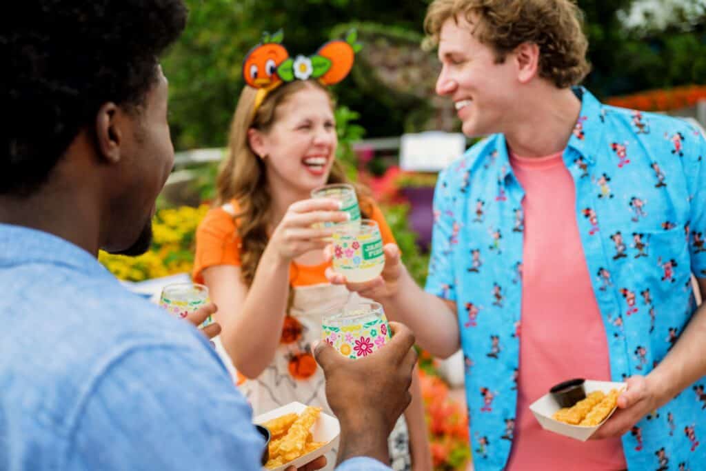 Friends enjoying colorful drinks and snacks at a Disney-themed outdoor event.