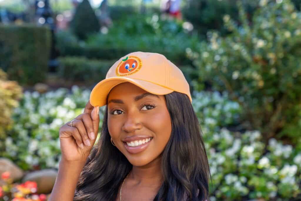 Woman wearing a bright yellow EPCOT Flower & Garden Festival hat outdoors.