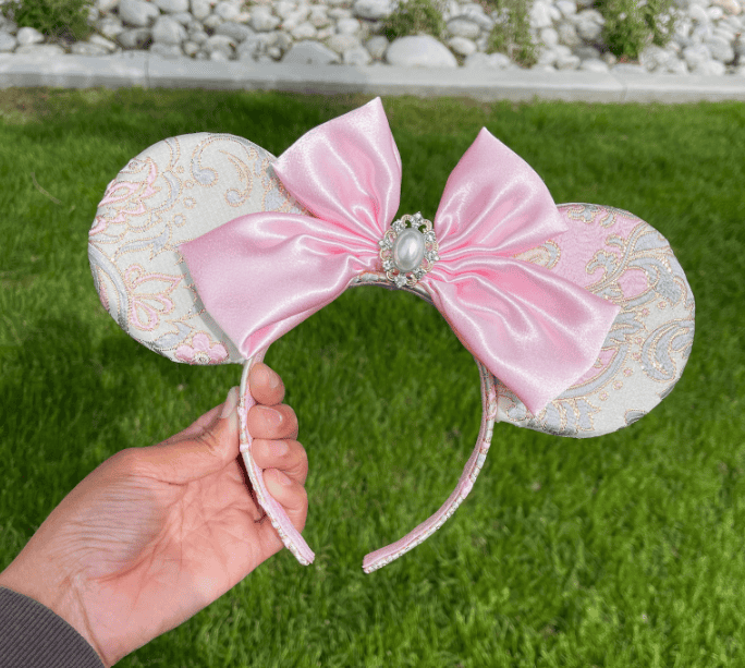 Pink coquette mouse ears headband with satin bow and pearl embellishment, perfect for Disney fans an.