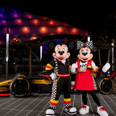 Mickey and Minnie Mouse in racing outfits at Disney theme park.