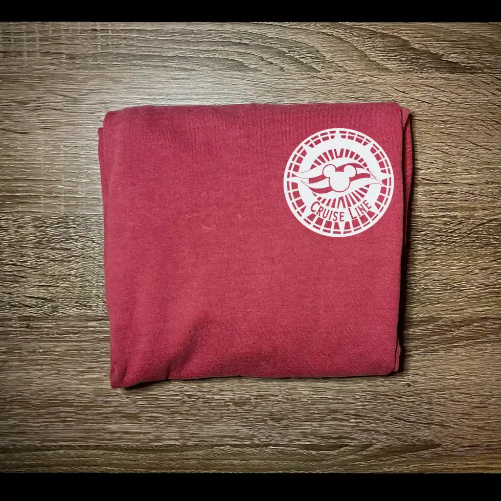 Pink Disney Cruise Line towel with logo on wooden surface.