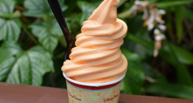 Orange soft-serve in a paper cup with a black spoon, set before lush greenery—a hidden Disney treat as magical as the parks themselves.