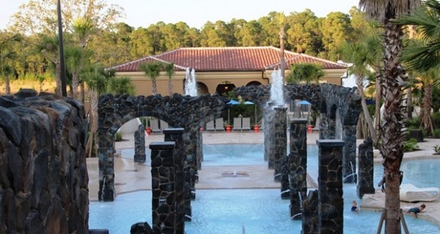 Elegant stone arches with fountains enhance a resort pool near Disney World, framed by palm trees and a luxury hotel.