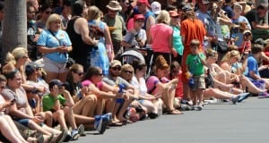 Disney fans gather along Main Street, many seated curbside, soaking up the sun and excitement as they await the parade.