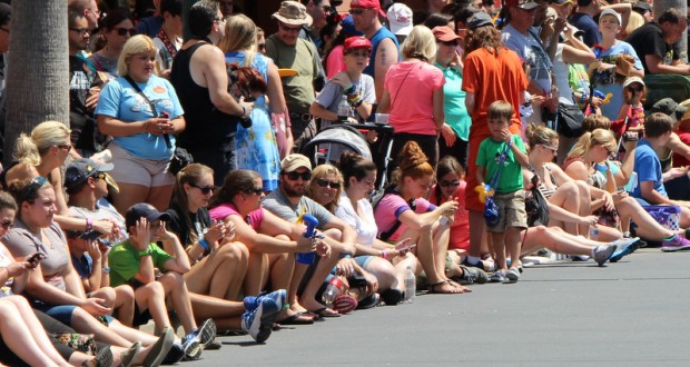 Disney fans gather along Main Street, many seated curbside, soaking up the sun and excitement as they await the parade.