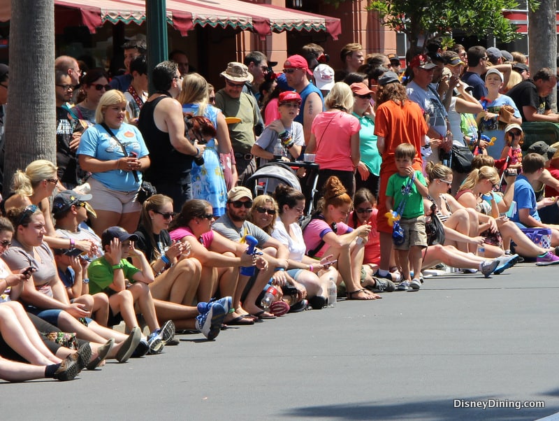 Disney fans gather along Main Street, many seated curbside, soaking up the sun and excitement as they await the parade.