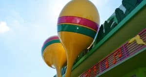Oversized yellow maraca sculptures with green and pink stripes greet guests outside a vibrant Disney World resort building.