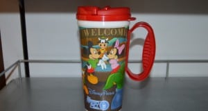 Disney Parks souvenir mug with red lid and handle, showcasing Mickey, Minnie, Goofy, and Pluto—ideal for Disney Parks fans.