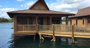 An overwater Disney bungalow with a whimsical patterned roof stands above the lake, evoking Polynesian Village Resort magic.
