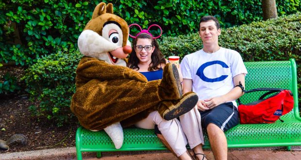 Two guests pose with Chip on a bench at Walt Disney World, all smiles as they capture their magical vacation moment.