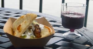 Gyro in a cardboard tray paired with red wine on a black table at Epcot, ready for Disney fans to savor during their visit.