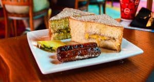 A plate with sausage links, pineapple, and powdered sandwich halves—fan-favorite Disney World treats for park-goers.
