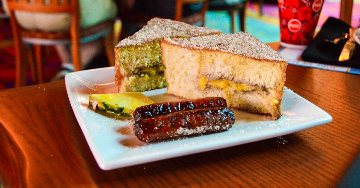 A plate with sausage links, pineapple, and powdered sandwich halves—fan-favorite Disney World treats for park-goers.