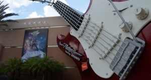 The iconic giant red and white guitar outside Rock 'n' Roller Coaster at Hollywood Studios, framed by palm trees and a mural.