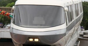 The iconic Disney World Monorail glides into the station, its sleek white and gray design framed by lush green trees.