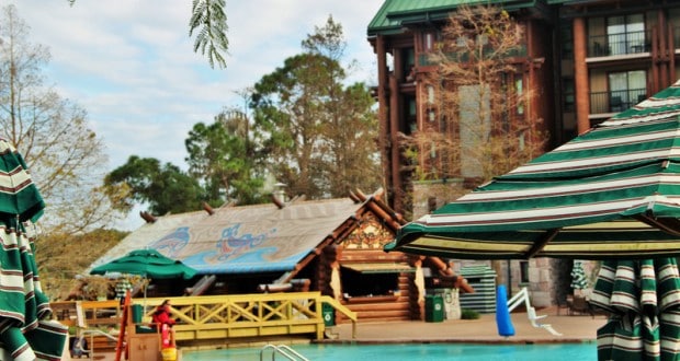 Charming poolside hangout at Disney's Wilderness Lodge with green-striped umbrellas and rustic log cabin ambiance.