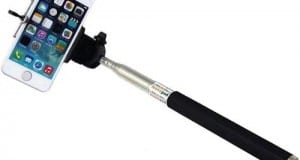 A smartphone on a black selfie stick with a wrist strap, showing its home screen—selfie sticks are not allowed at Disney World.