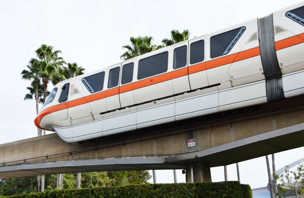 The iconic white and orange Disney monorail glides above lush palms, inviting guests to the wonder of working at Disney parks.