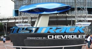 Test Track presented by Chevrolet sign and sleek blue car sculpture greet guests at Epcot’s high-speed Disney World attraction.