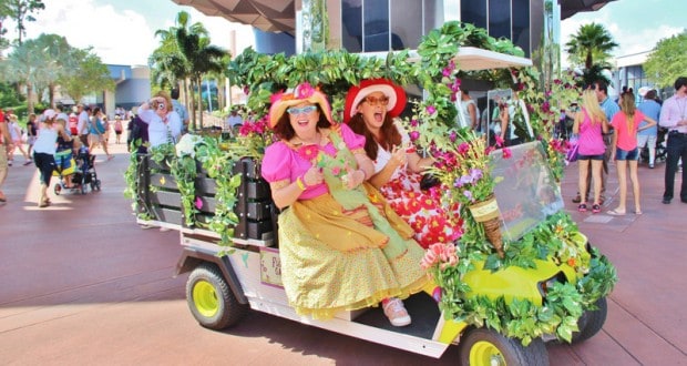 Cast Members in vibrant floral costumes and hats cruise Epcot in a flower-adorned golf cart, capturing Disney magic at work.