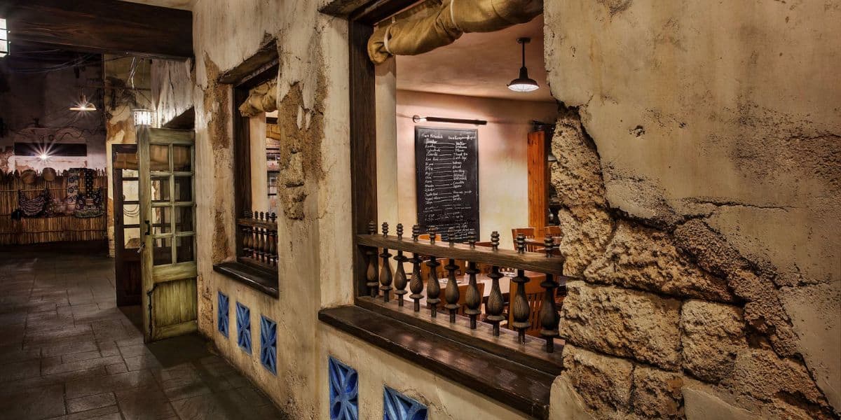 Rustic restaurant interior with worn stucco walls and wooden accents. Open windows reveal dim lighting and a chalkboard menu inside. The exterior has a weathered look, creating a cozy and vintage atmosphere.