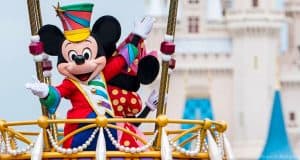 Mickey Mouse in a vibrant parade costume waves from his float before Cinderella Castle at Disney World, thrilling park guests.