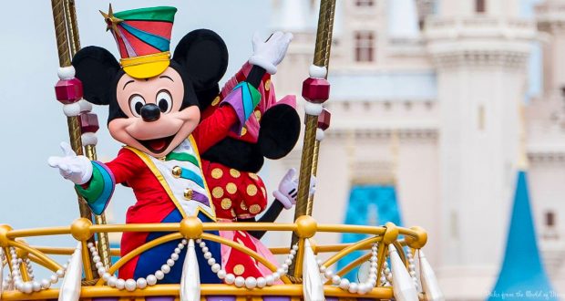 Mickey Mouse in a vibrant parade costume waves from his float before Cinderella Castle at Disney World, thrilling park guests.