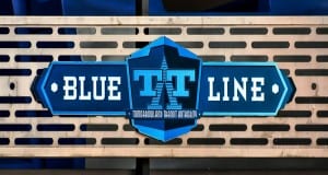 BLUE LINE" sign with Tarrant Transit Authority logo on a metal fence, blue seats behind—like Disney signs guiding park guests.
