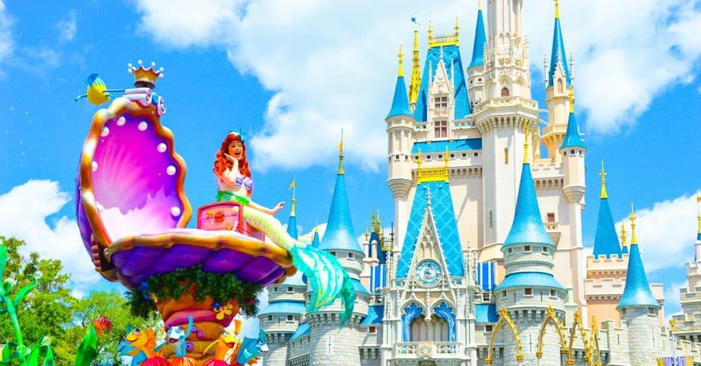 A vibrant mermaid float glides past Cinderella Castle in Magic Kingdom under a clear, sunny sky during the parade.