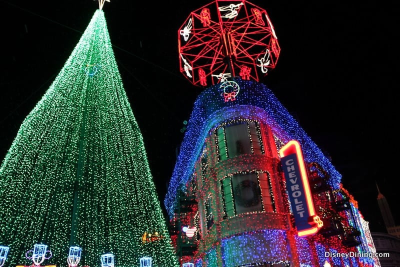A giant Christmas tree and building glowing with vibrant lights, plus a red Chevrolet sign evoke classic Osborne Lights at Disney World.