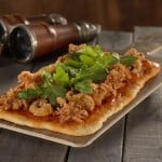 Adventure-themed rectangular pizza with fried calamari and arugula at Jock Lindsey’s Hangar Bar, beside compass and telescope.