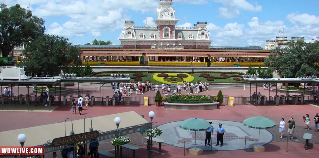 Magic Kingdom entrance with colorful Mickey Mouse floral display, excited guests, and Main Street train station—Disney magic awaits!.