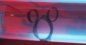 A glass reflection reveals a classic Hidden Mickey silhouette with big ears, set against vibrant red and blue Disney colors.