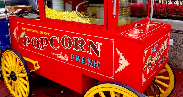Classic Disney snack vibes: a bright red popcorn cart with yellow wheels and fun lettering, serving fresh popcorn at Disney World.