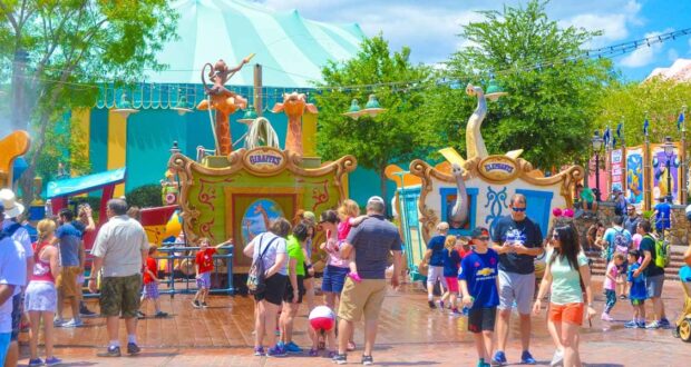 Guests stroll through a vibrant, circus-themed section of Disney World, soaking in the park’s lively atmosphere on a sunny day.