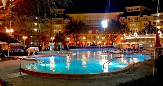 Disney resort pool glowing at night, with a whimsical white carousel horse and lounge chairs creating magical vacation vibes.