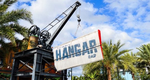 A crane installs the iconic Hangar Bar sign among palm trees at Disney Springs, signaling a new hotspot for Disney fans.