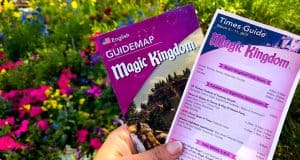Magic Kingdom guidemap and times guide held up, surrounded by vibrant flowers—your ticket to an epic Walt Disney World adventure.