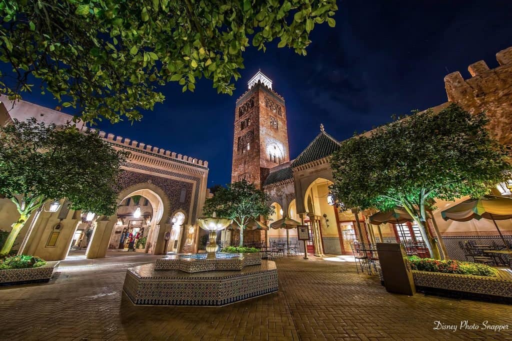 Epcot’s Morocco Courtyard at night, glowing with warm lights, tiled fountain, arches, and a soaring tower—an immersive Disney gem.