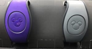 Purple and gray Disney MagicBands with Mickey Mouse icons, side by side on black, hint at the magic awaiting guests in the parks.