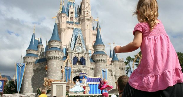 A young guest rides on shoulders, enjoying a dazzling castle show amid the lively crowds at Walt Disney World.