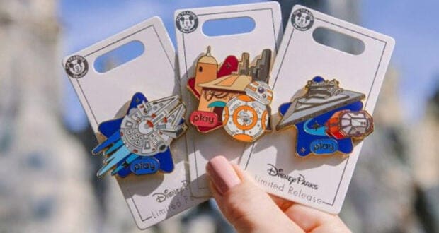 A hand holds three Disney Parks limited release Star Wars pins featuring the Millennium Falcon, BB-8, and a Star Destroyer—essential finds for any collector following Disney Shopping Tips. Each pin is on a white display card with colorful designs and the word "play.