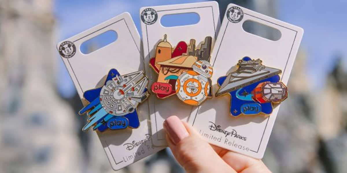 A hand holds three Disney Parks limited release Star Wars pins featuring the Millennium Falcon, BB-8, and a Star Destroyer—essential finds for any collector following Disney Shopping Tips. Each pin is on a white display card with colorful designs and the word "play.