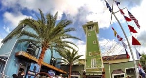 The Boathouse at Disney Springs dazzles with its green tower, waving flags, and palm trees greeting guests at the entrance.