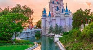 A magical castle by a shimmering moat, framed by lush trees at sunset, evokes Disney World’s enchanting vacation vibe.